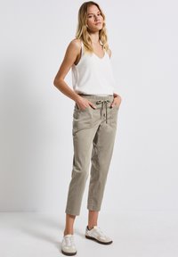 Lätta, beige joggerbyxor med elastisk midja, dragsko och sidofickor, kombinerat med en vit ärmlös topp och sneakers.