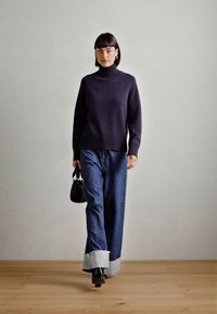 Jūras spēku turtleneck dzemperis, džinsu platā kāju bikses ar kontrastējošiem gaišajiem apkaklītes galiem, melna soma, valkāta ar papēža zābakiem. Minimalistiska dizaina.