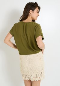 Top de manga corta verde oliva combinado con una falda de encaje de crochet color crema que presenta patrones hexagonales y un dobladillo con picos.