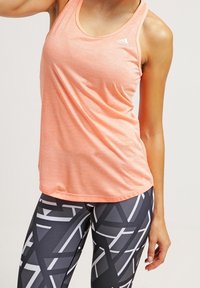 Lys orange atletisk top med rund udskæring og tynde stropper, parret med sorte leggings med et geometrisk gråt mønster.