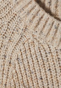 Tissu de pull en tricot beige avec un motif côtelé texturé. Contient des éclats de couleurs plus foncées et une apparence confortable et épaisse.