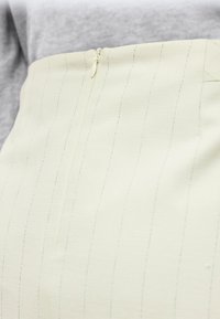 Κρεμ φούστα με ψηλή μέση, λεπτές κάθετες ρίγες και κρυφό φερμουάρ στο πίσω μέρος, φορεμένη με γκρι τοπ.