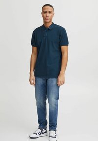 T-shirt polo bleu marine avec un col, une patte de boutonnage sur le devant et des manches courtes, associé à un jean clair et des baskets noir et blanc.
