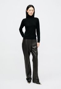 Suéter preto de gola alta feito de tecido macio, combinado com calças de couro pretas de cintura alta que apresentam uma textura suave e um ajuste elegante.