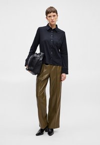 Črna srajca z dolgimi rokavi, teksturirana tkanina; v kombinaciji z olivno zelenimi hlačami širokega kroja z visokim pasom in črnimi škornji na peto.