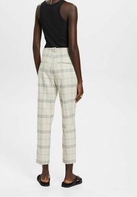 Crème geruite broeken hebben een gestructureerde pasvorm, een cropped lengte en een hoge taille. Ze hebben een gladde textuur en subtiele rode en zwarte accenten.
