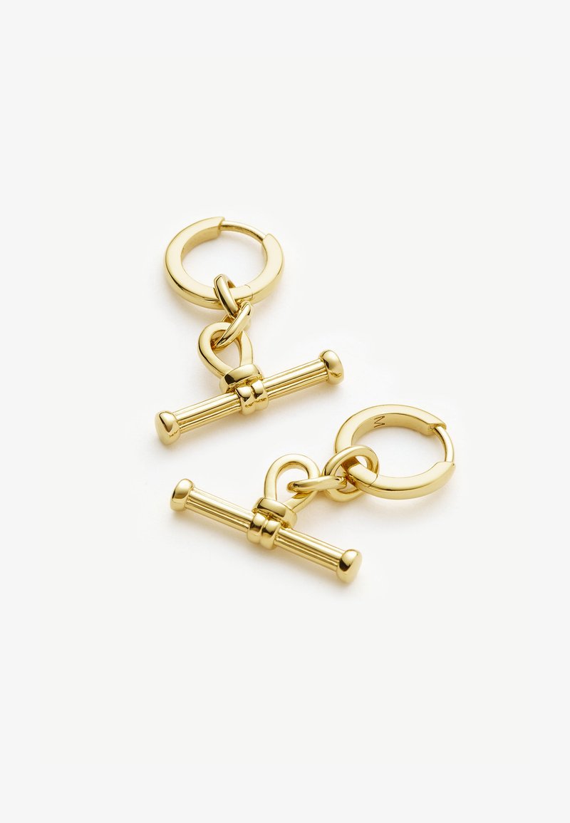 Náušnice z kovu v zlatej farbe, ktoré obsahujú kruhový krúžok a dekoratívny dizajn s opaskom so predĺženými prízvukmi. Hladký povrch a lesklý finiš.