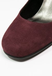 Gros plan sur une chaussure plate pour femme en daim bordeaux avec un bout arrondi et une semelle noire sur fond blanc.