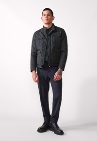 Black quilted jacket featuring two chest pockets, a high collar, and a zip closure, paired with dark pants and black boots.