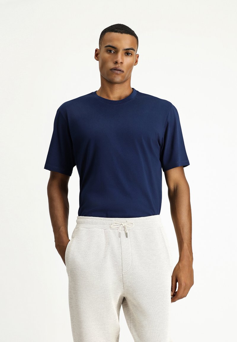 T-shirt blu navy a maniche corte con scollo rotondo, abbinato a pantaloni grigi chiari con texture, dotati di vita elastica e cordoncino.