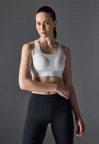 Hvit sports-BH med firkantet utringning, teksturert stoff og formede kopper, kombinert med svarte høyhalsede leggings.