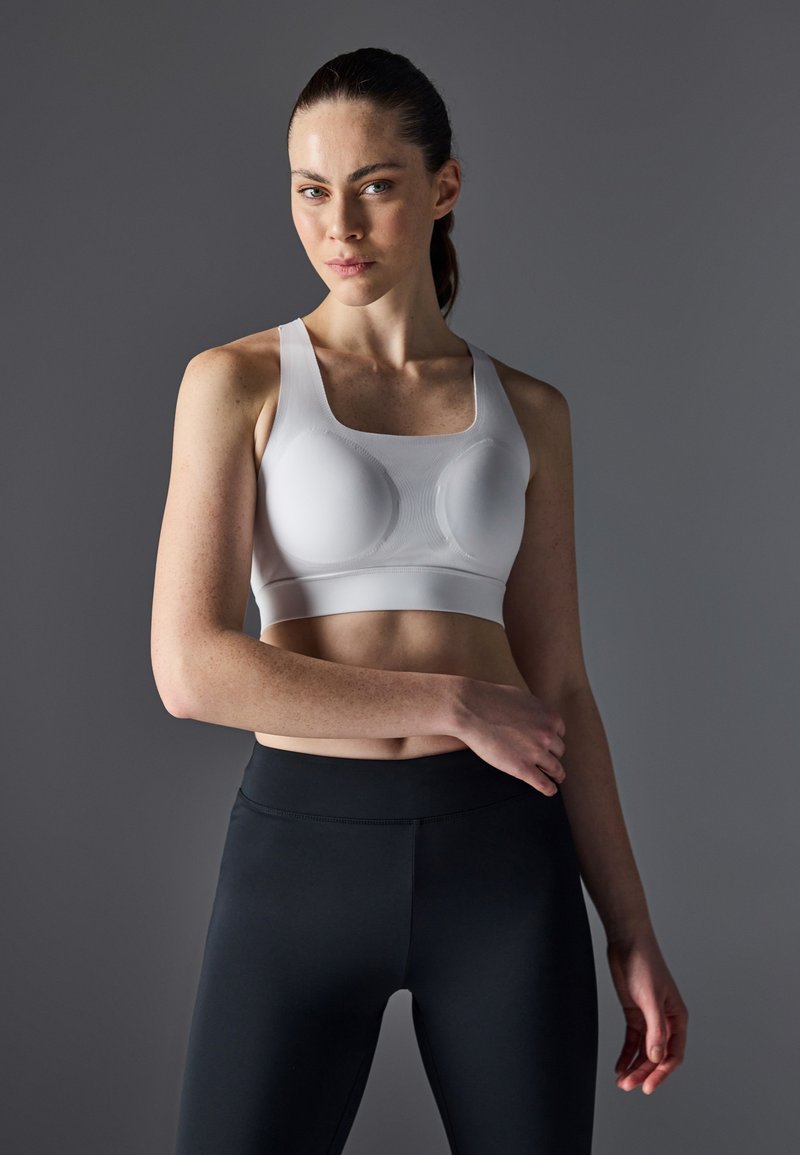 Hvit sports-BH med firkantet utringning, teksturert stoff og formede kopper, kombinert med svarte høyhalsede leggings.