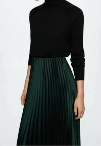 Black knitted turtleneck sweater paired with a long, pleated, dark green satin skirt, emphasizing texture and flow.