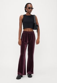 Svart cropped tank top, lilla fløyels brede bukser, svarte chunky støvler og en tilbehørsveske. Modell som bærer solbriller og teksturerte øreringer.