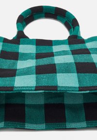 Miękka tote bag z czarno-tealowym dużym wzorem w kratę i okrągłymi uchwytami na białym tle.