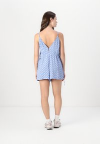 Mono azul con estampado, con un respaldo en forma de V, tirantes ajustables, cintura elástica y pantalones cortos, hecho de una tela ligera.