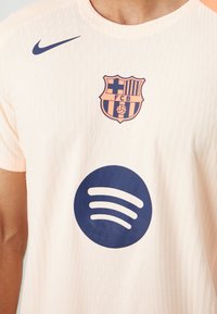 White football jersey with FC Barcelona crest, navy Nike logo on right chest, and large navy Spotify logo in center.