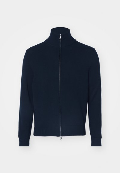 Temno modra zip jopica s visokim ovratnikom, rebrastimi manšetami in robom. Narejena iz mehkega pletenega materiala. Srebrna zadrga je okrasna na sprednji strani.