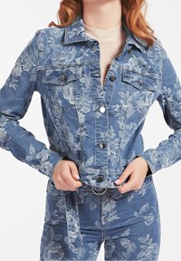 Giacca in denim con motivo floreale, colore azzurro chiaro, due tasche sul petto, bottoni a pressione e dettagli con vita rifinita.