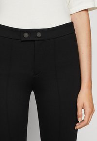 Zwarte slimfit broek met een gladde textuur, uitgerust met een platte tailleband, twee ronde knopen en zijnaaddetails voor een op maat gemaakte uitstraling.