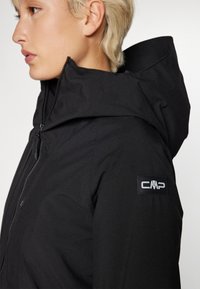 Black waterproof jacket with a high collar, zip closure, and a CMP logo on the sleeve. Textured fabric with a smooth finish.