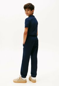 Navyblauw polo shirt gecombineerd met bijpassende joggingbroek, voorzien van een elastische tailleband, zijzakken en beige sneakers met veters.
