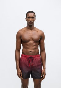 Ανδρικό μαγιό με μπαντζάκια σε διαβαθμισμένο σχέδιο, από κόκκινο σ�ε μαύρο· ελαστική μέση με κορδόνι· εμφανές λογότυπο στη πλευρά.