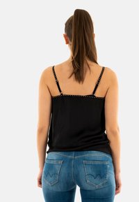 Débardeur noir avec des clous décoratifs sur les bretelles, associé à un jean bleu avec un design de couture de poche distinctif.