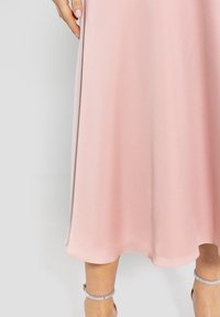 Długa, zwiewna sukienka w kolorze blush róż z gładkiego materiału o subtelnej poświacie; z falbaniastym dołem i eleganckim układem.