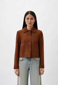 Bruine suède cropped jas met een kraag, sluiting met knopen aan de voorkant en twee opgestikte zakken. Gekocht over lichtblauwe denim jeans.