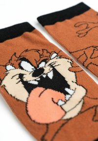 Calzini marroni con il volto di un personaggio dei cartoni animati, con un polsino nero, decorati con dettagli bianchi e arancioni, che mostrano un'espressione giocosa.