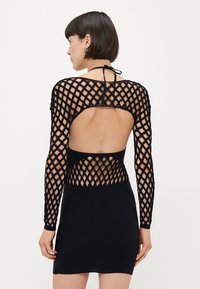Abito nero con silhouette aderente, maniche lunghe con motivo in rete, design con schiena scoperta e chiusura a cravatta al collo.