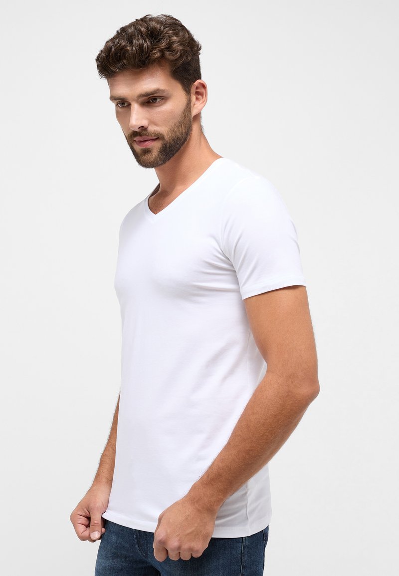 Hvid kortærmet V-hals t-shirt lavet af glat stof, tætsiddende design og med subtile sømme; båret med blå denim jeans.