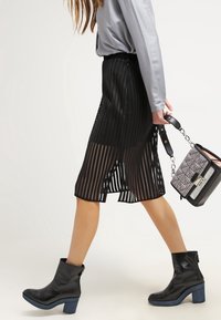 Svart mesh-midi kjol med vertikala ränder, i kombination med en ljusgrå långärmad topp och svarta ankelboots med blå klackar.