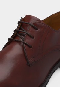 Chaussure habillée en cuir marron avec des lacets marron foncé et des coutures détaillées, montrant les parties avant supérieure et latérale.