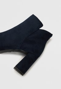 Mornja plava antilop čizma do članka s širokim blok petom i jedinstvenim prorezom na članku. Glatka tekstura bez vidljivih hardverskih detalja.