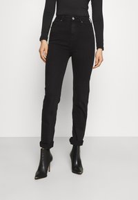 Jeans negros de tiro alto con un corte slim, dobladillos enrollados y cierre frontal de botones; combinados con botas de tacón negras hasta el tobillo.
