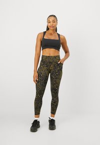 Sujetador deportivo negro combinado con leggings de cintura alta que presentan un patrón abstracto multicolor en tonos oscuros. Zapatillas deportivas negras completan el look.