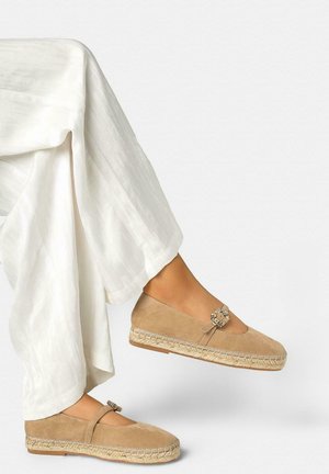 Benen met brede witte broek en beige suède espadrille platte schoenen met decoratieve gespbanden.