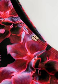 Virágmintás textil élénk piros és rózsaszín virágokkal fekete háttérrel. Az élén egy kis arany logó díszítés található.