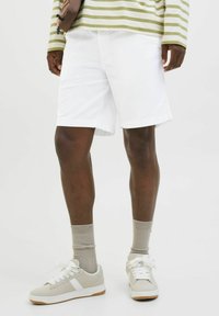 Pantalones cortos blancos de corte recto, combinados con zapatillas ligeras grises y calcetines beige. La parte superior presenta rayas verdes y blancas.