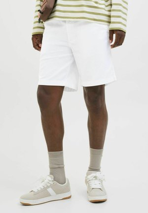 Witte shorts met een rechte snit, gecombineerd met lichtgrijze sneakers en beige sokken. Het bovenstuk heeft groene en witte strepen.