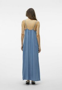 Abito lungo in denim chiaro, con sottili spalline, schiena arricciata, texture morbida e orlo dritto che arriva fino alle caviglie.