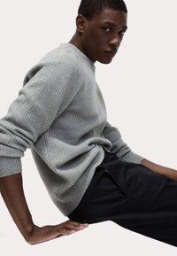 Suéter texturizado gris claro con cuello redondo y puños acanalados, combinado con pantalones negros que tienen bolsillos laterales y un detalle de botón.