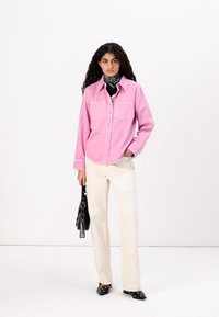 Pink corduroy button-up shirt with two chest pockets, paired with cream trousers. Accessories include a black handbag and patterned scarf.