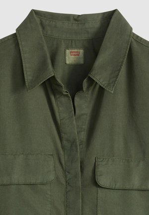Chemise boutonnée vert olive avec un col à revers, deux poches poitrine et un tissu en coton lisse. Comprend une étiquette au niveau du col.