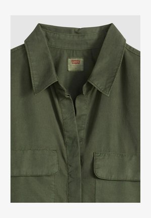 Chemise boutonnée vert olive avec un col à revers, deux poches poitrine et un tissu en coton lisse. Comprend une étiquette au niveau du col.