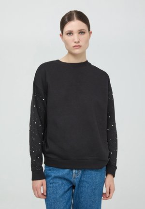 Felpa nera con maniche lunghe e decorazioni a forma di perle. Collo rotondo classico e vestibilità rilassata. Abbinata a jeans in denim blu.