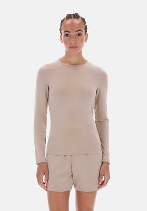 Beige pitkähihaisen yläosan, jossa on pyöreä pääntie, pehmeää kangasta ja tiukka istuvuus, yhdistetty samansävyisiin beigeihin shortseihin.