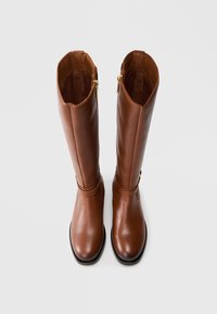 Bottes hautes en cuir marron aux genoux avec une finition lisse, fermetures éclair latérales et un bout arrondi. Un détail de sangle est placé au-dessus de la cheville.